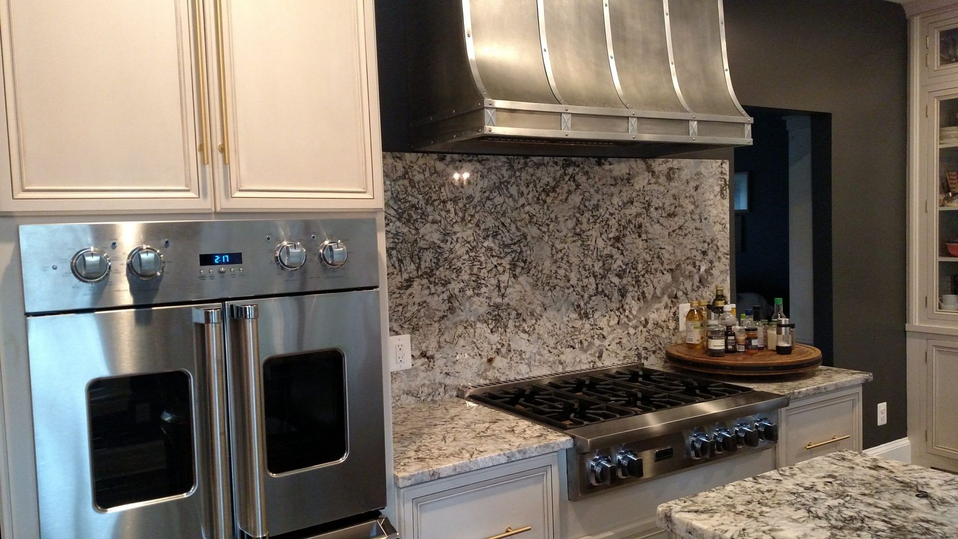 Modern kitchen with stainless steel double oven, gas range, mosaic backsplash, and granite countertops