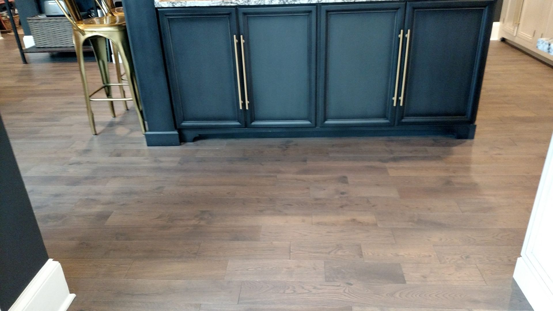 Dark blue kitchen island cabinets with brass handles on a hardwood floor in a room.