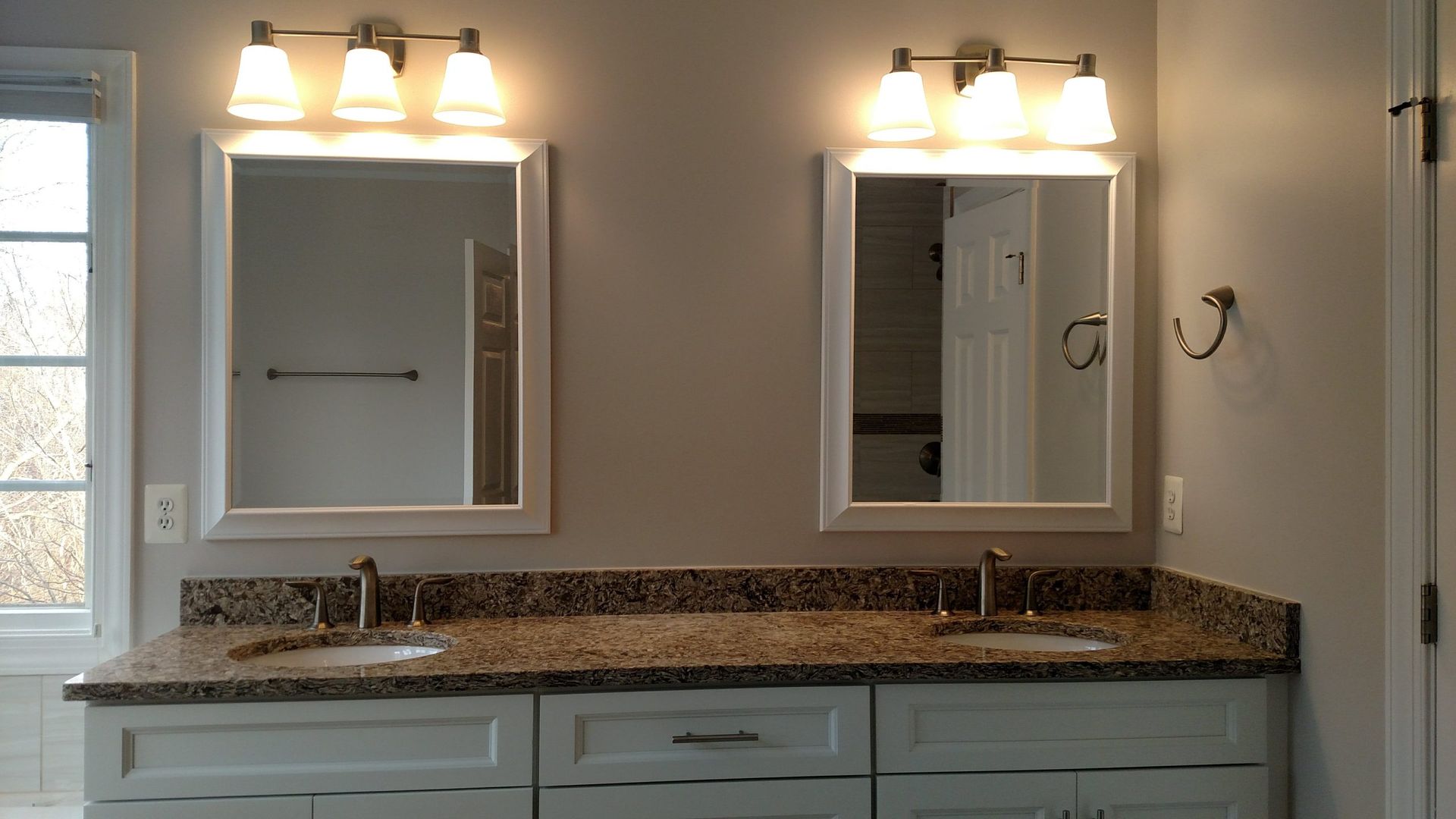 Double vanity bathroom with granite countertop, two mirrors, and warm lights above.