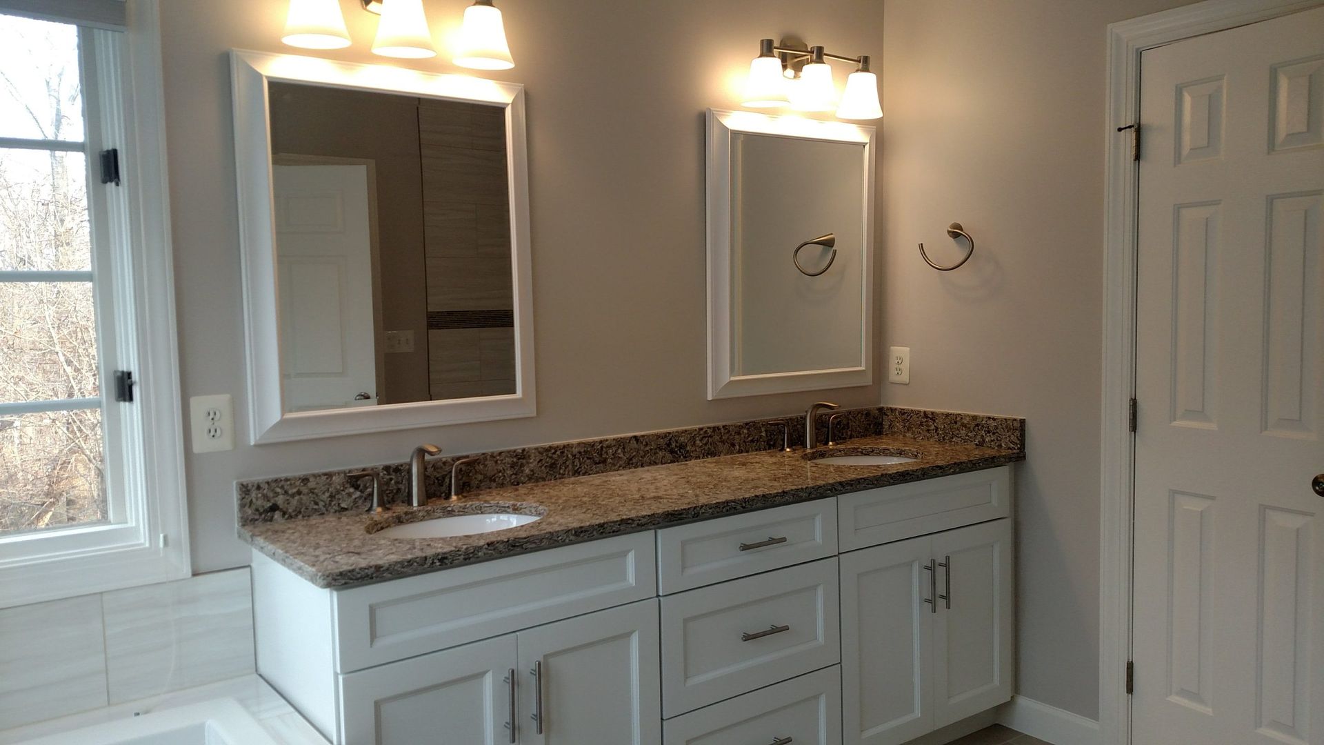 Bright bathroom vanity with double mirrors, granite countertop, wall lights, and a white shower curtain