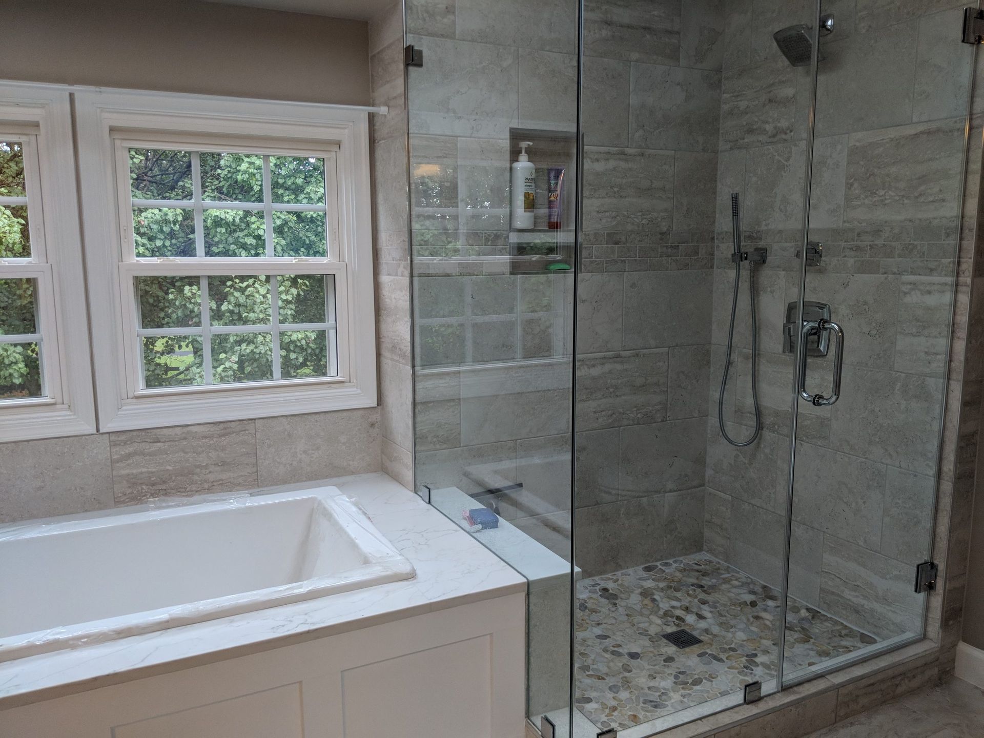 Bathroom with white tub, glass shower enclosure, and marble tile walls and floor.