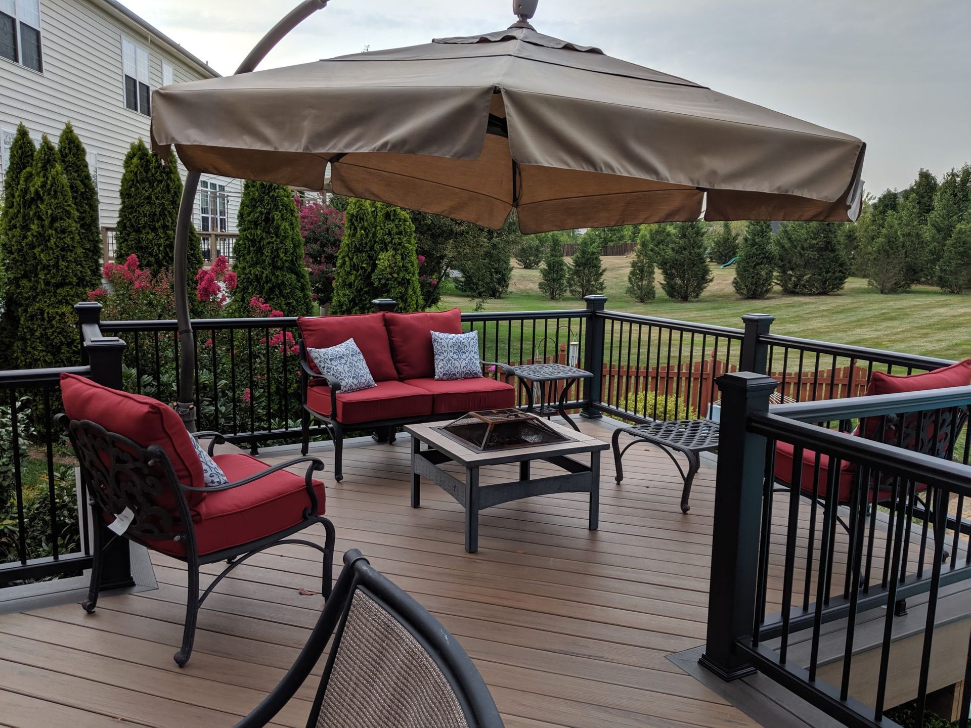 Patio with red cushioned seating, tan umbrella, and black metal railing overlooking a grassy yard