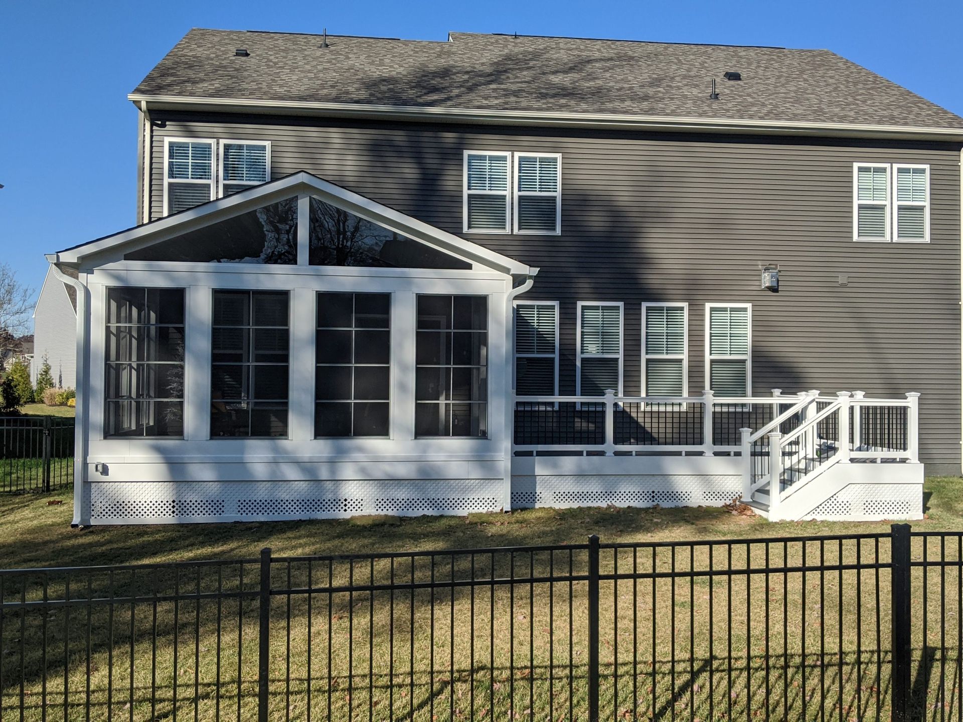 Gray house with a screened porch, white trim, and a black fence in front under a blue sky