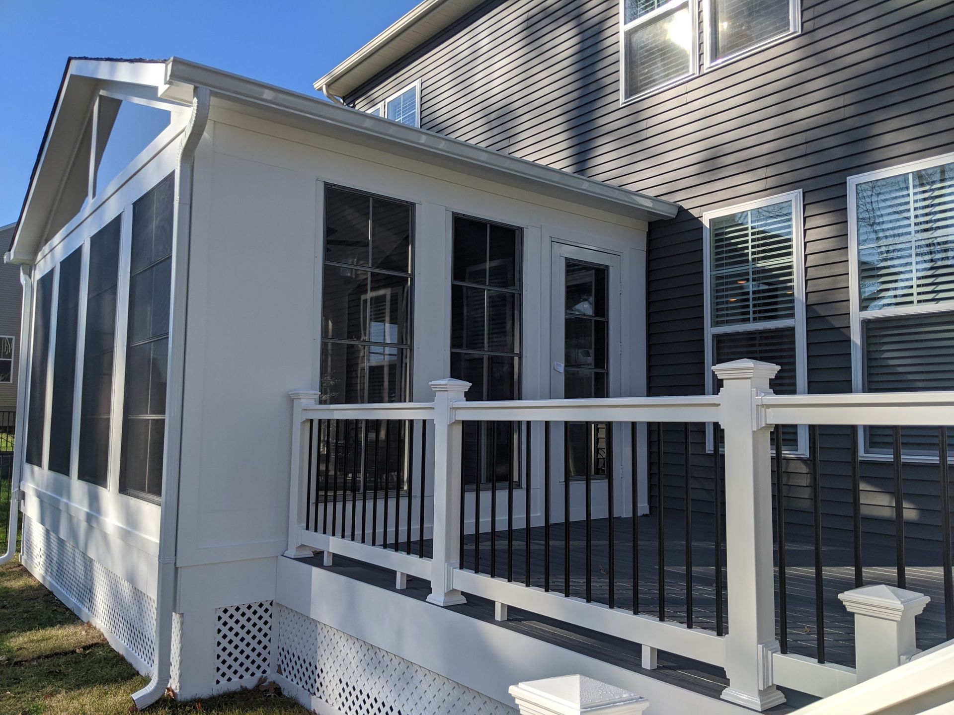 White screened porch attached to a house, with black railings and a glass door