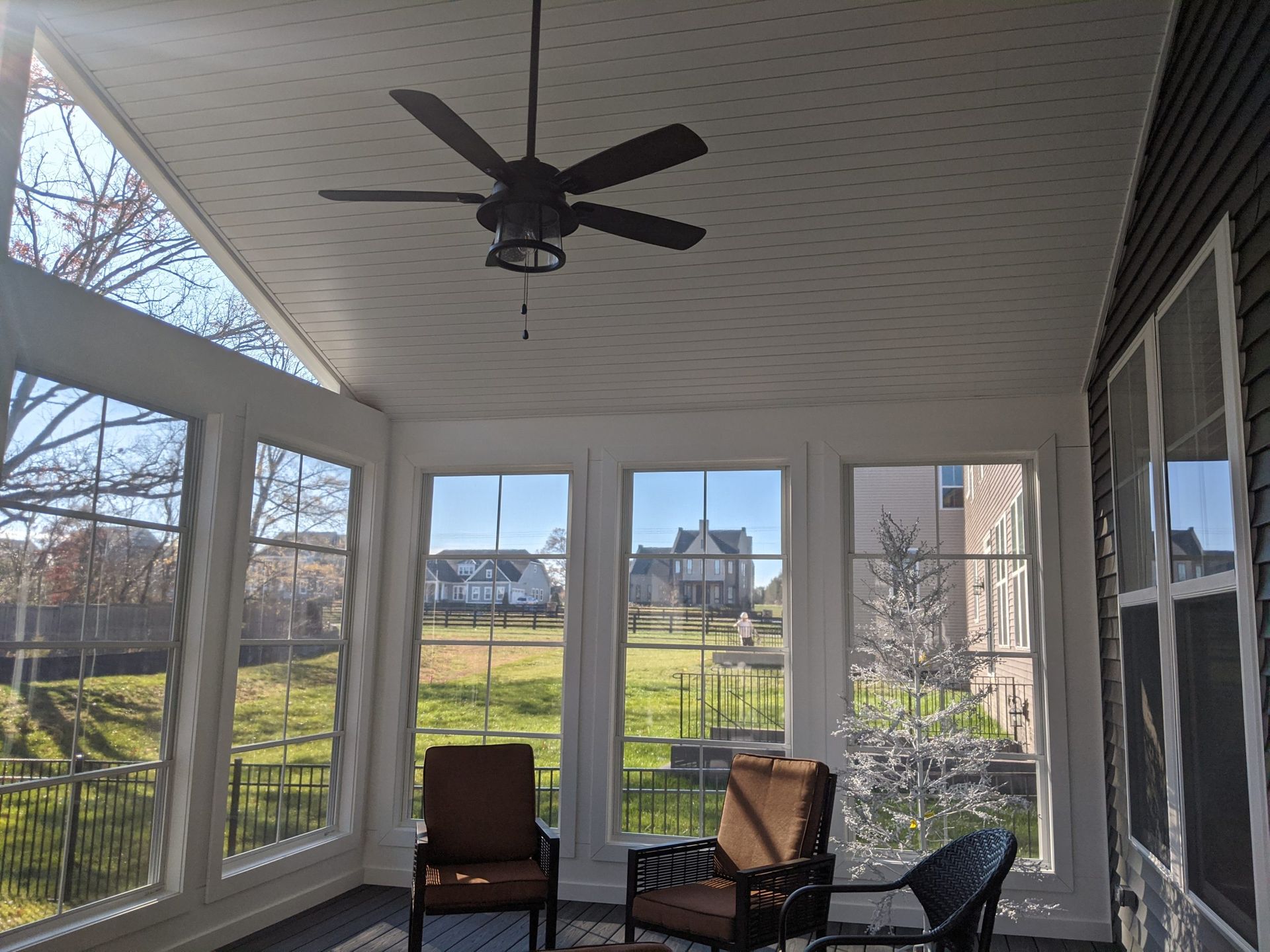 Sunroom with wicker chairs, ceiling fan, and large windows overlooking a backyard and neighboring houses