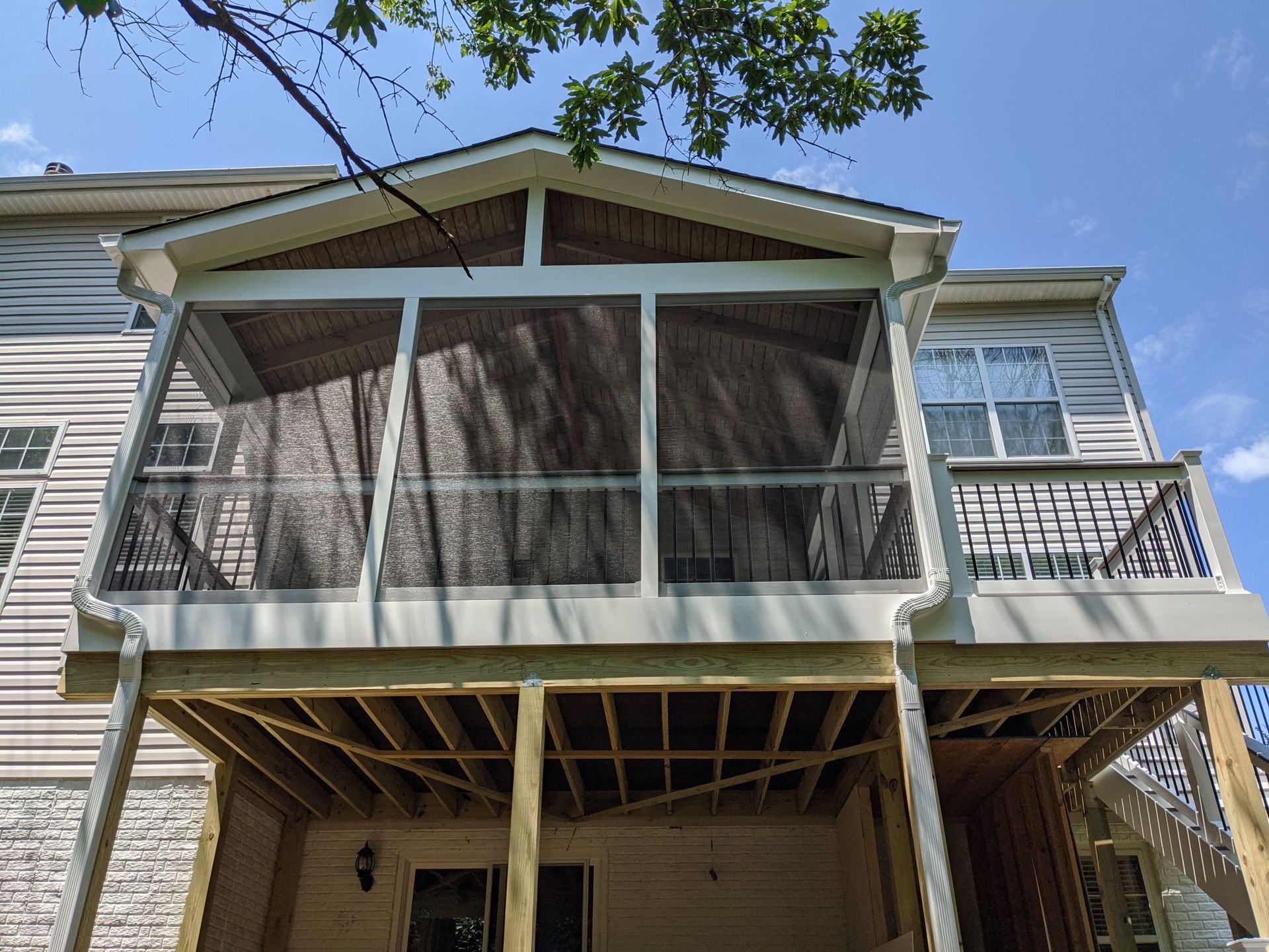 Screened porch on a two-story house with white trim and a small balcony under a blue sky