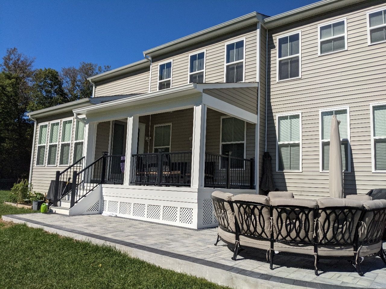 Back patio with white siding house, screened porch, and black metal fire pit on a sunny day
