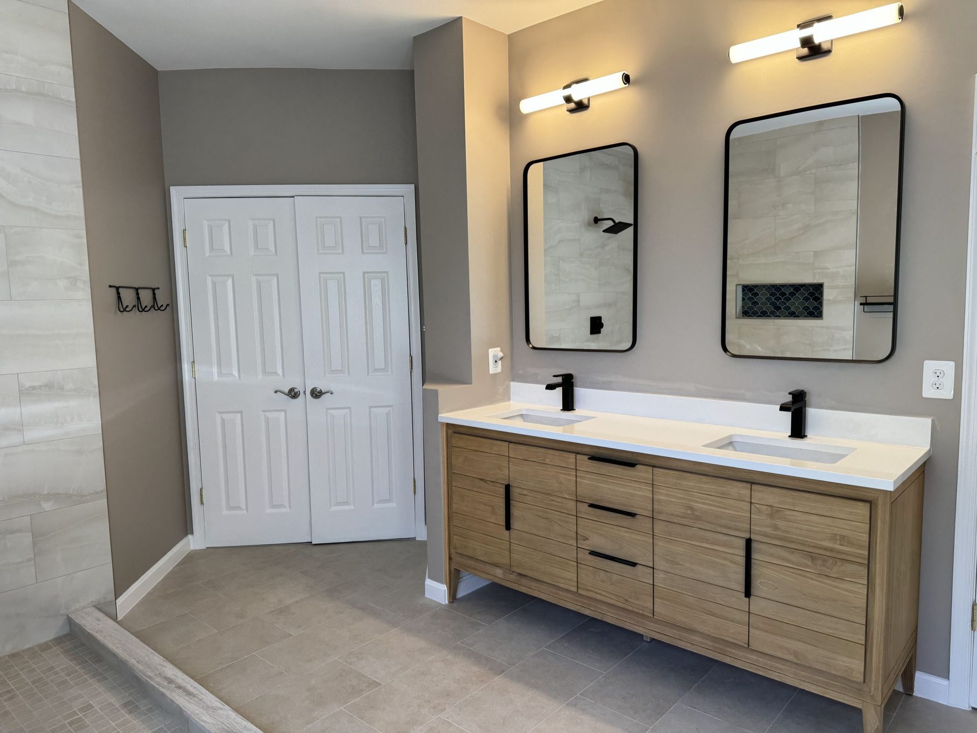 Bathroom vanity with double mirrors, wall lights, and white double doors in a beige-toned room