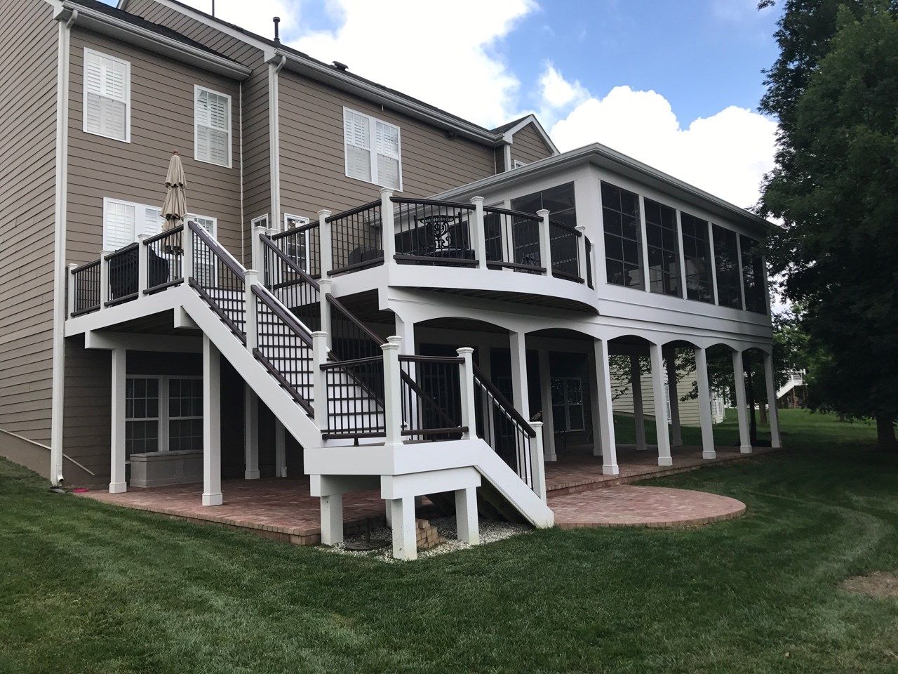 Backyard deck with white stairs, black railings, and covered patio beside a brick house.