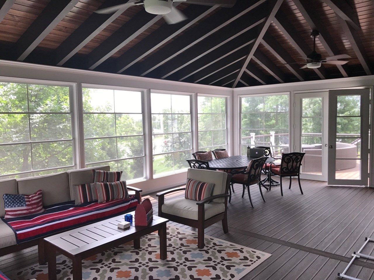 Screened porch with wooden beams, striped bench, chairs, table, and outdoor garden views