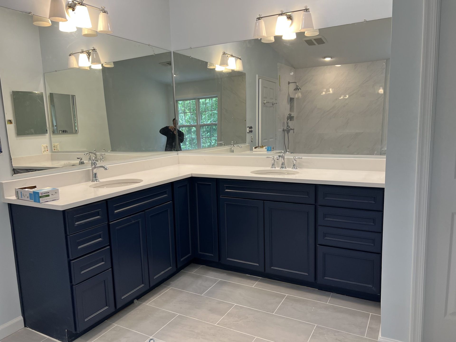 Bathroom vanity with large mirrors, white countertops, and navy cabinets under pendant lights.