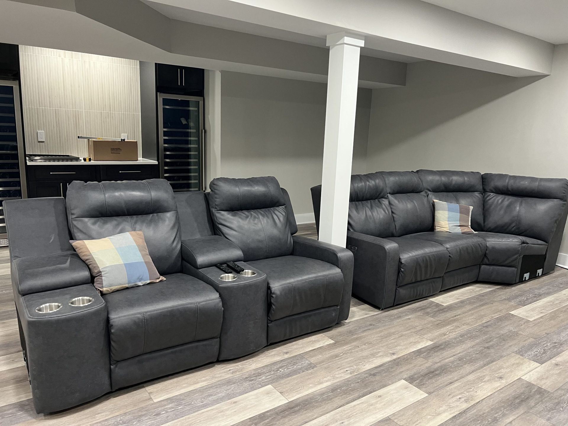 Basement lounge with three black recliner sofas on wood-look flooring and a white support column