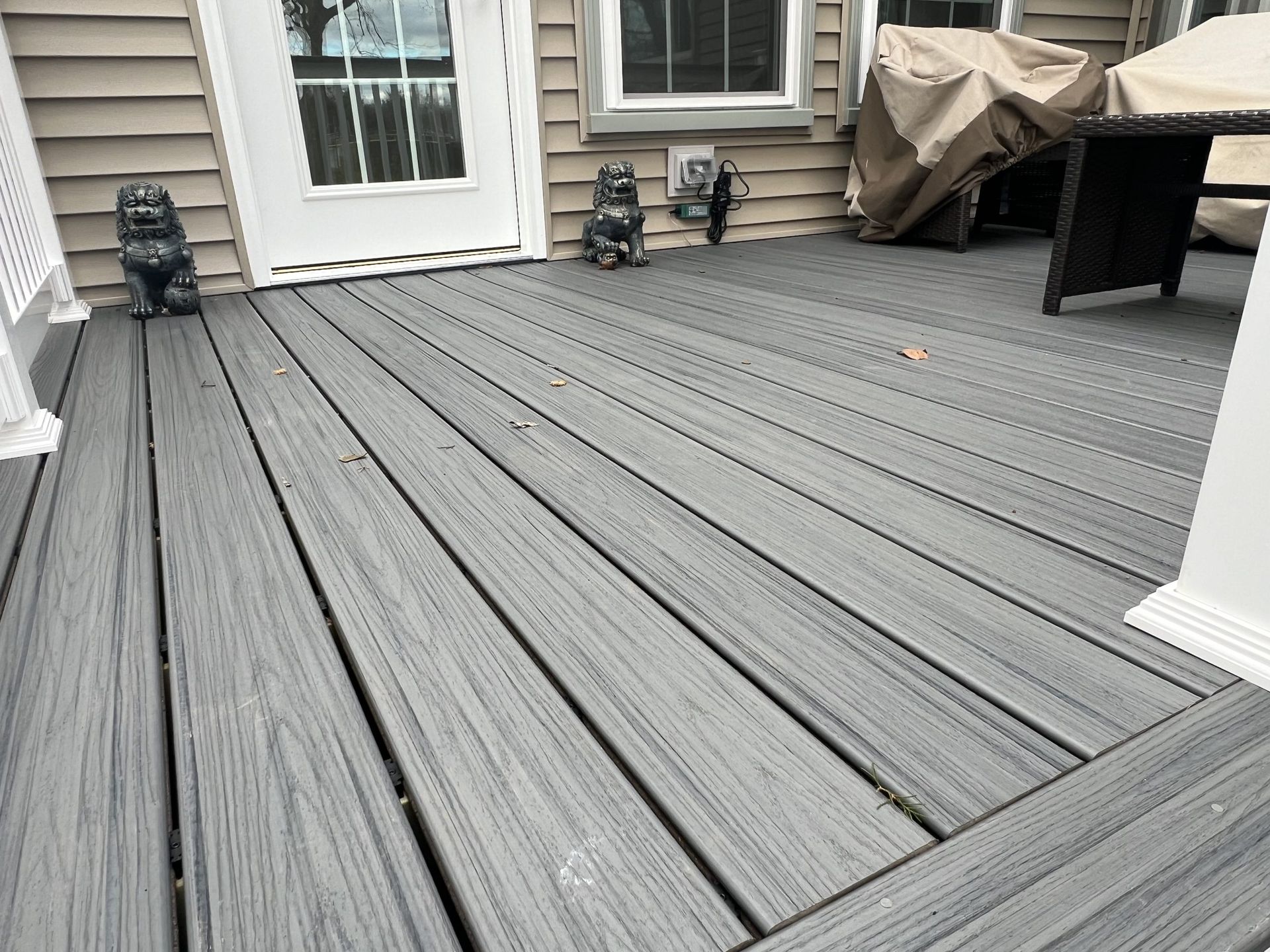 Gray composite deck with patio chairs, a covered grill, and sliding door outside a house