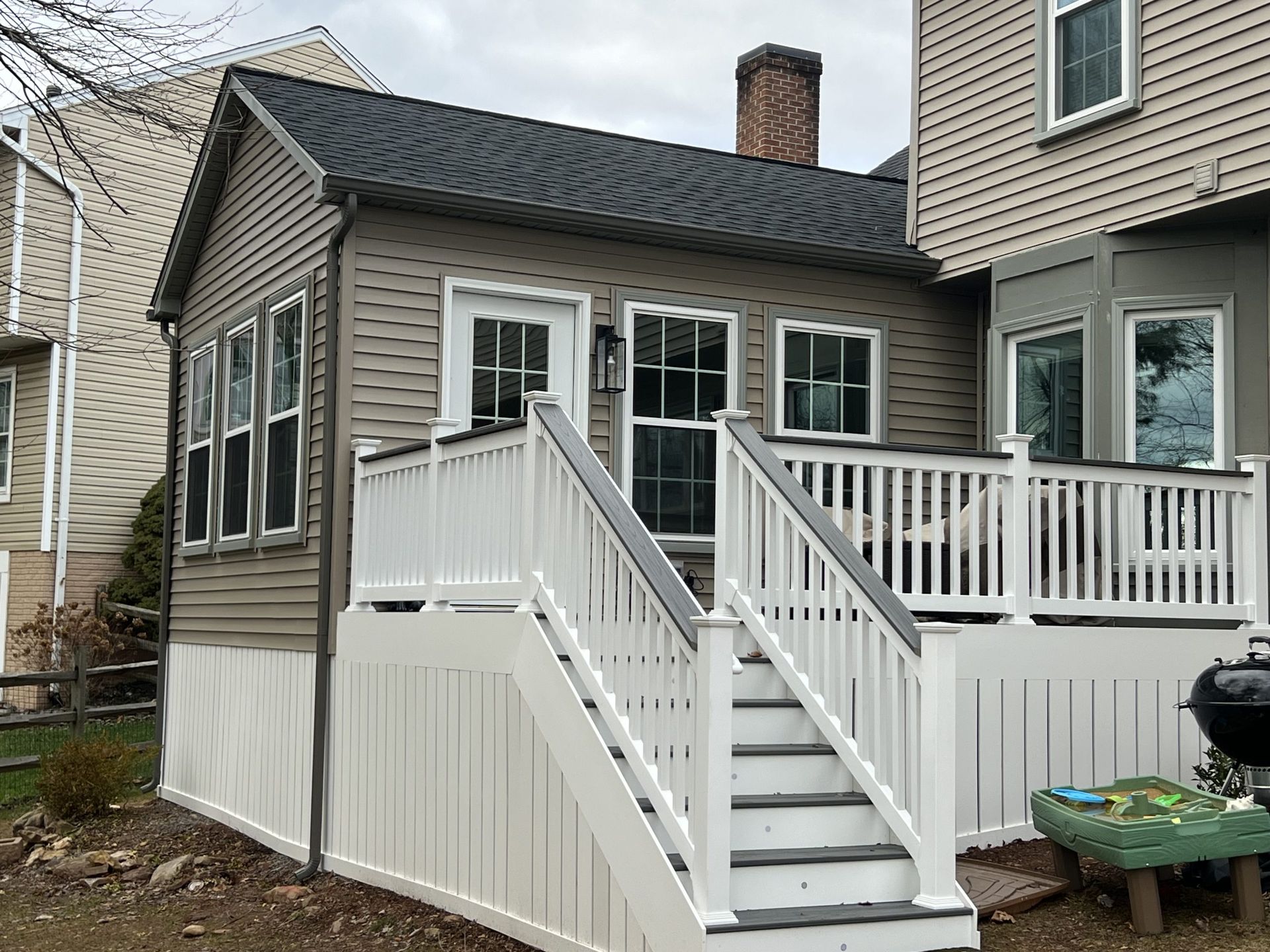 Small house rear deck with white railings, stairs, and a side entrance in a residential yard.