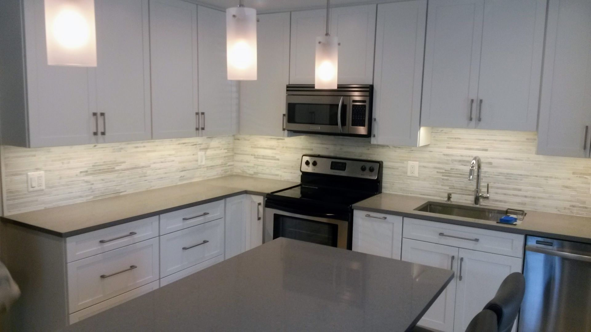 Modern kitchen with gray cabinets, white backsplash, black appliances, and a central island.
