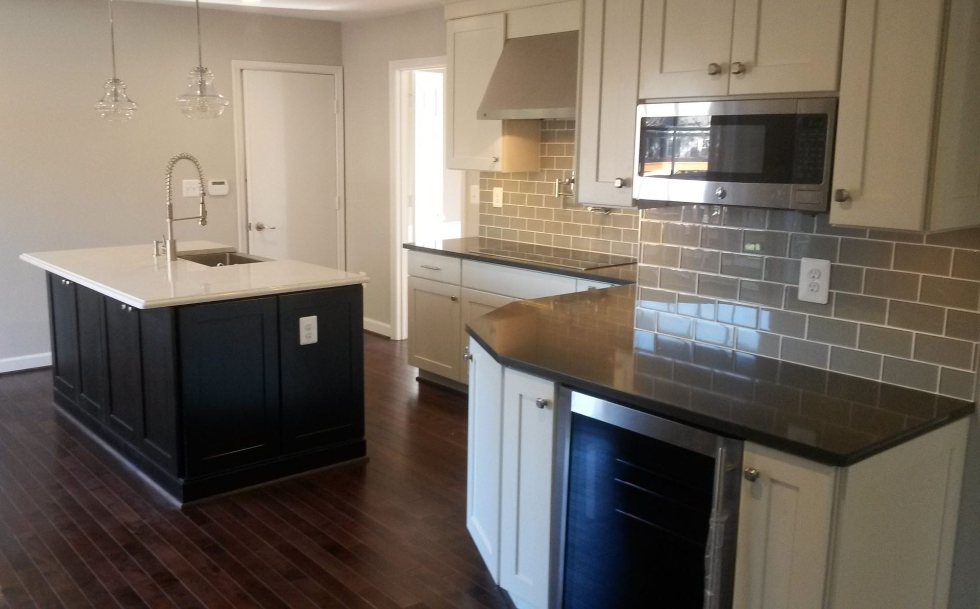 Modern kitchen with dark island, white cabinets, stainless appliances, and dark hardwood floors.
