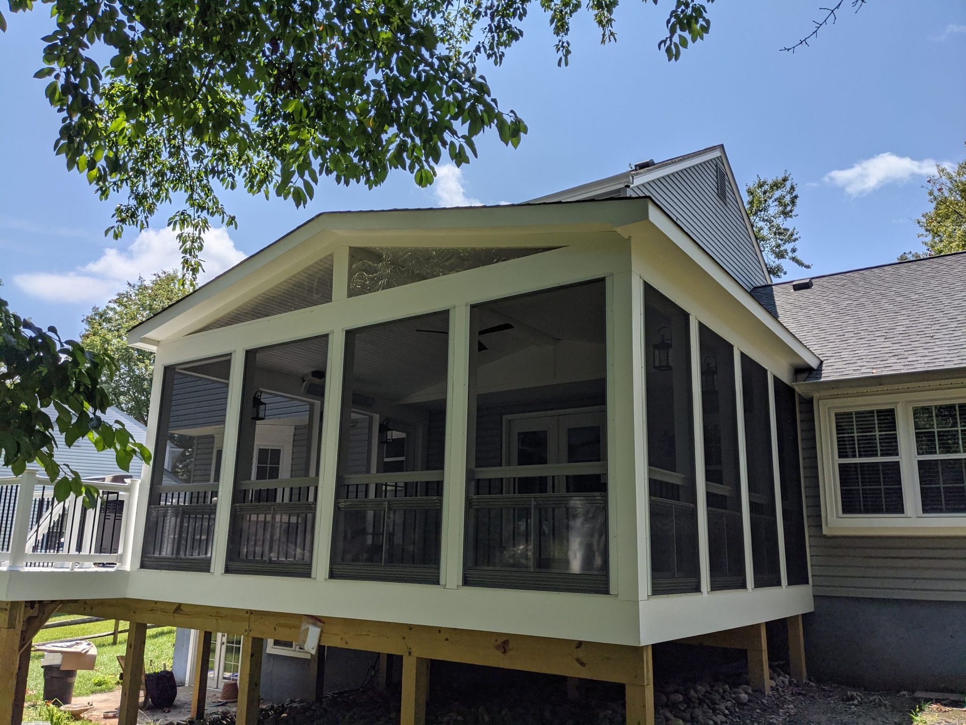 Screened porch with pale yellow trim and dark railings on a house, viewed from the yard