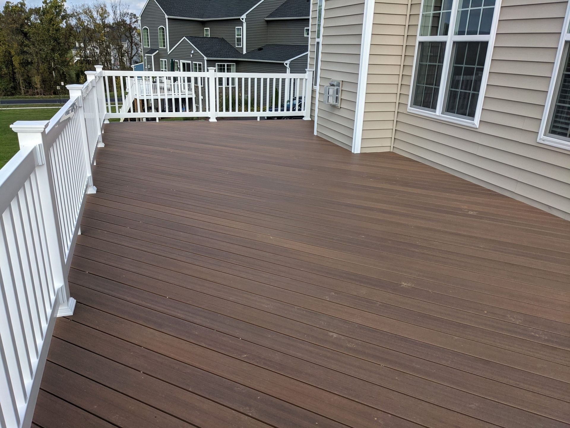 Wooden backyard deck with white railing and beige house siding