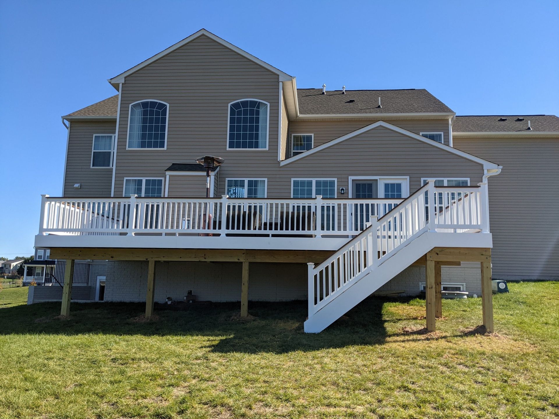 Two-story house with a large white deck and stairs in a grassy yard under a blue sky