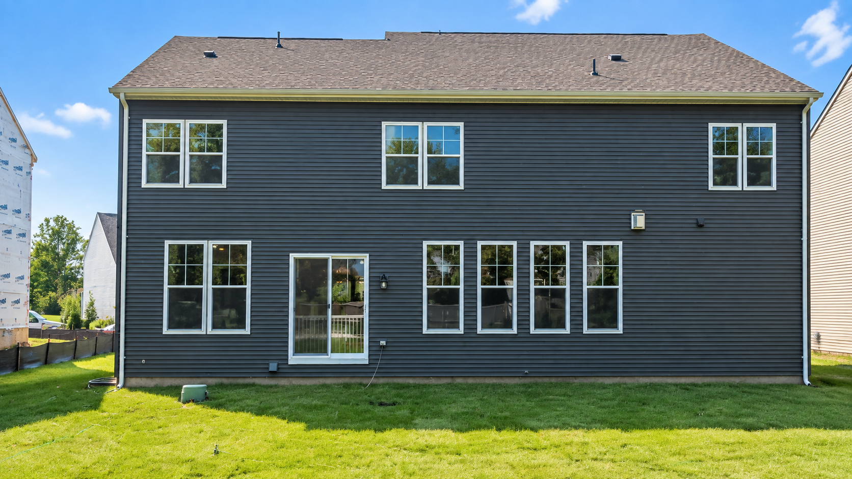 Two-story dark gray house with white-trimmed windows and a grassy backyard under a blue sky