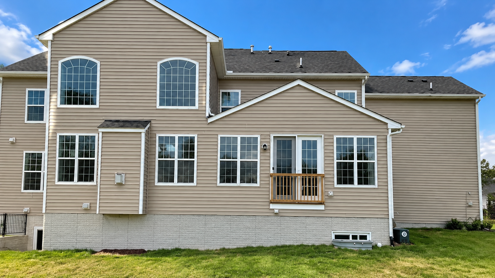 Tan two-story suburban house with white trim and multiple windows on a grassy lot