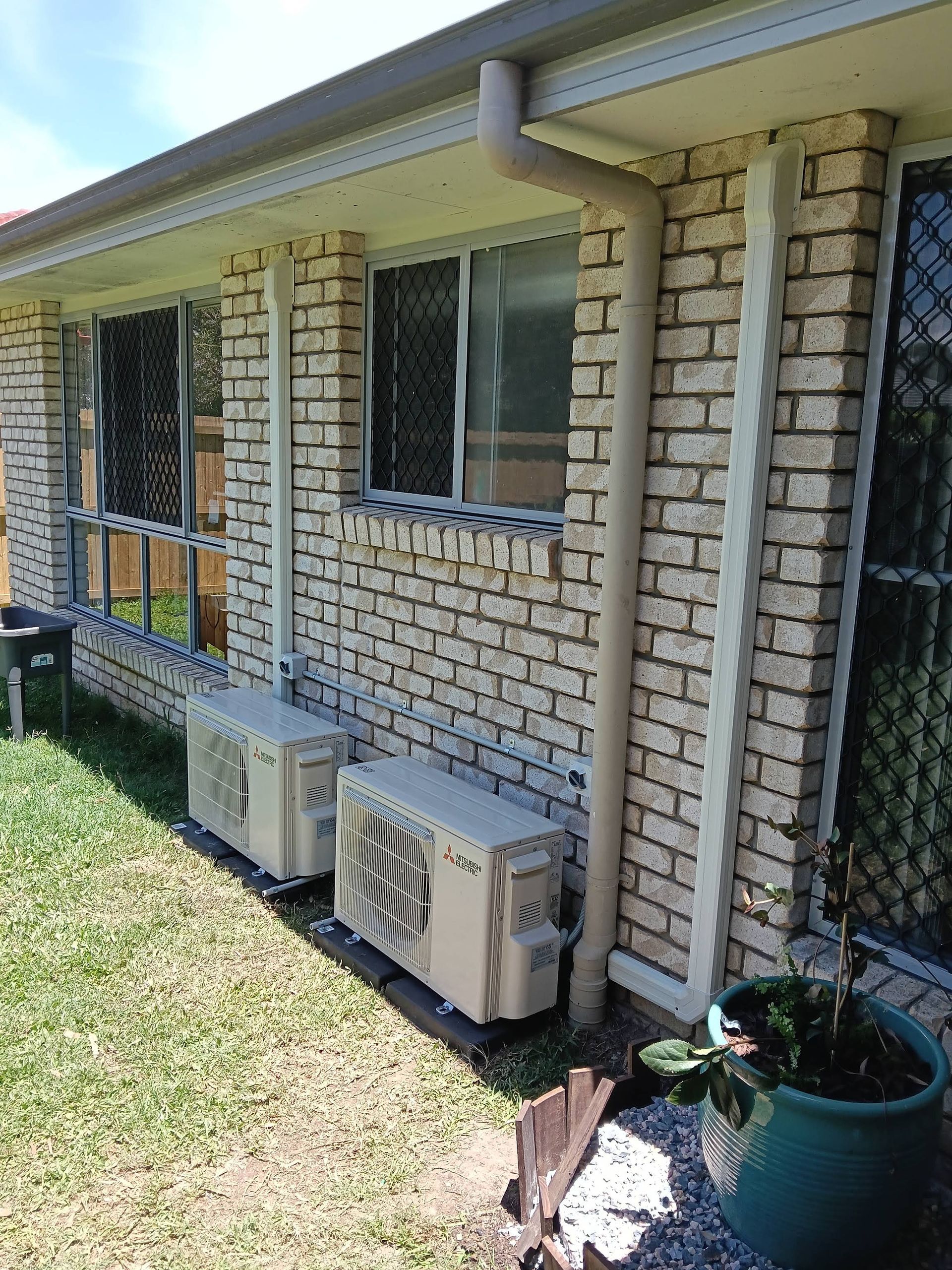 Two Beige Air Conditioning Units Mounted on a Brick Wall Beneath Windows — DC Active Electrical in Brighton, QLD