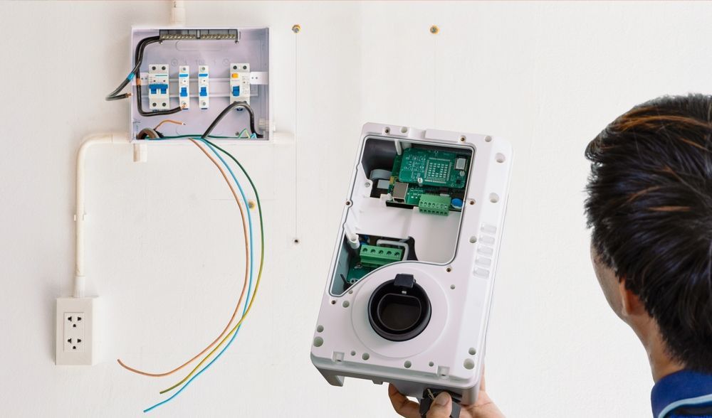 Person Installs an Electrical Box Component on a White Wall — DC Active Electrical in Brighton, QLD