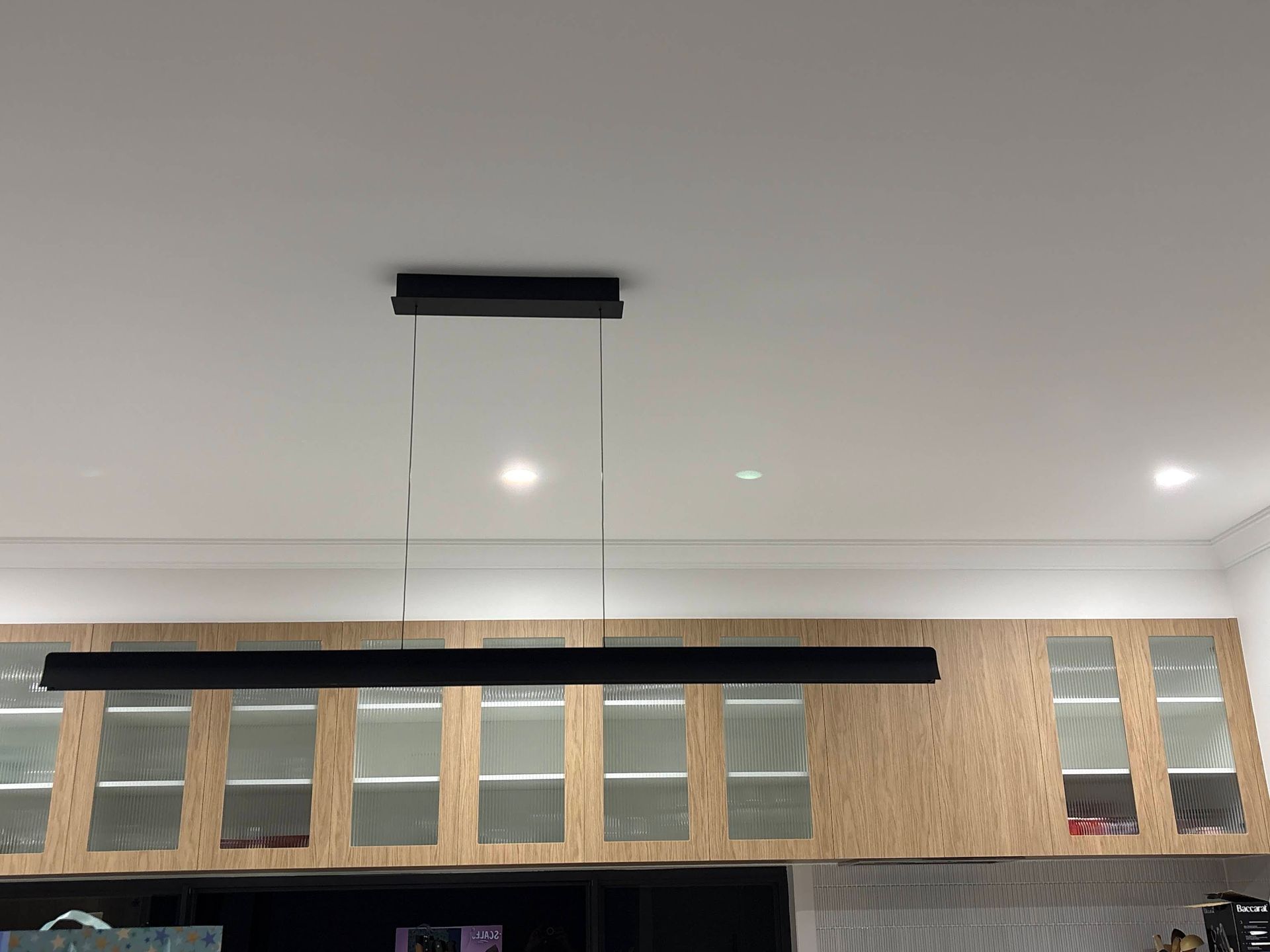 Black Rectangular Pendant Light Hanging Above Kitchen Cabinets With Glass Doors — DC Active Electrical in Brighton, QLD