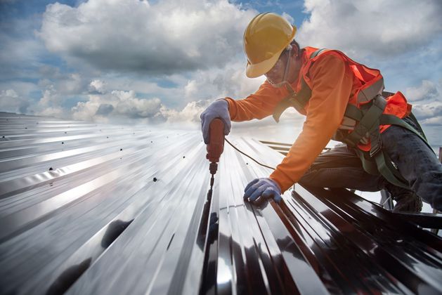 Worker in hard hat inspecting rooftop solar panels under a cloudy sky