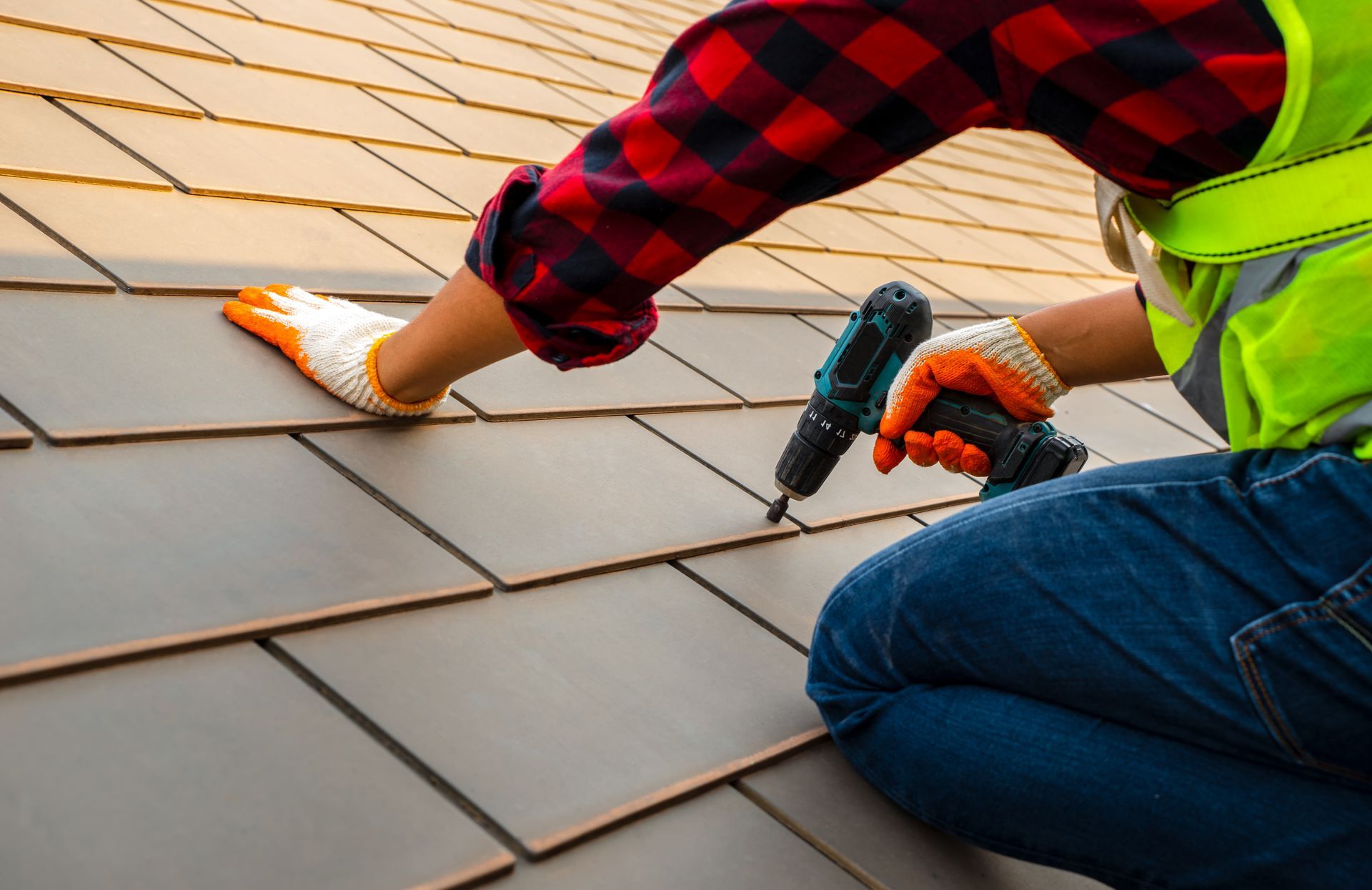 Roofing worker installing shingles with a nail gun on a sloped roof