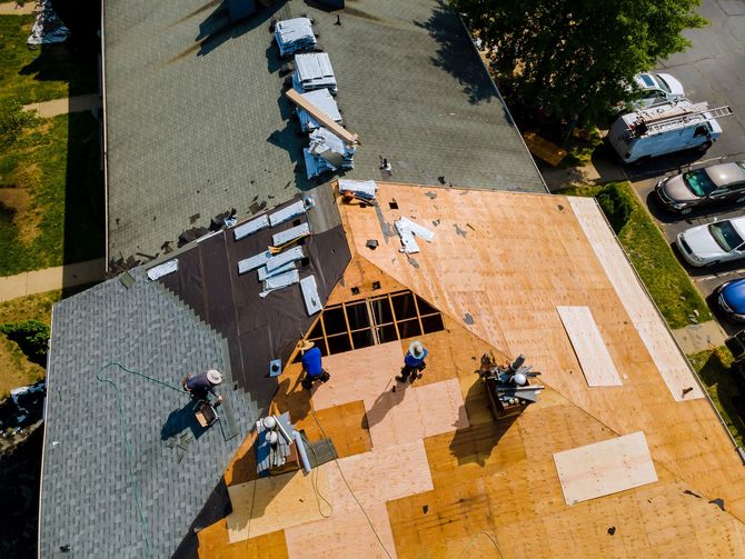 Roofers repairing a house roof with plywood sheets and tools, seen from above.