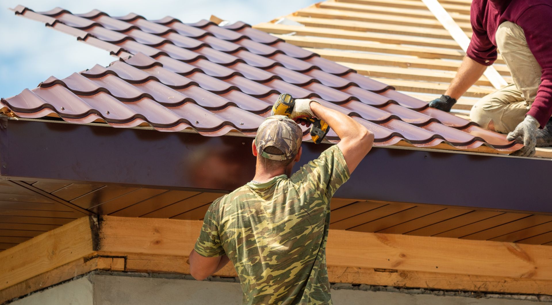 Two workers installing red roof tiles on a house roof
