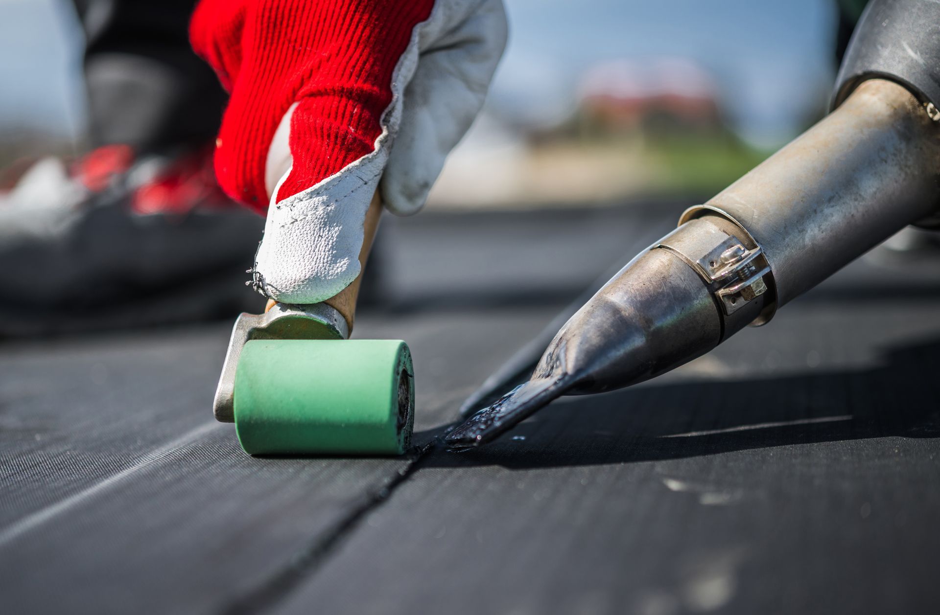 Gloved hand rolling green coating onto a black roof seam with a metal applicator