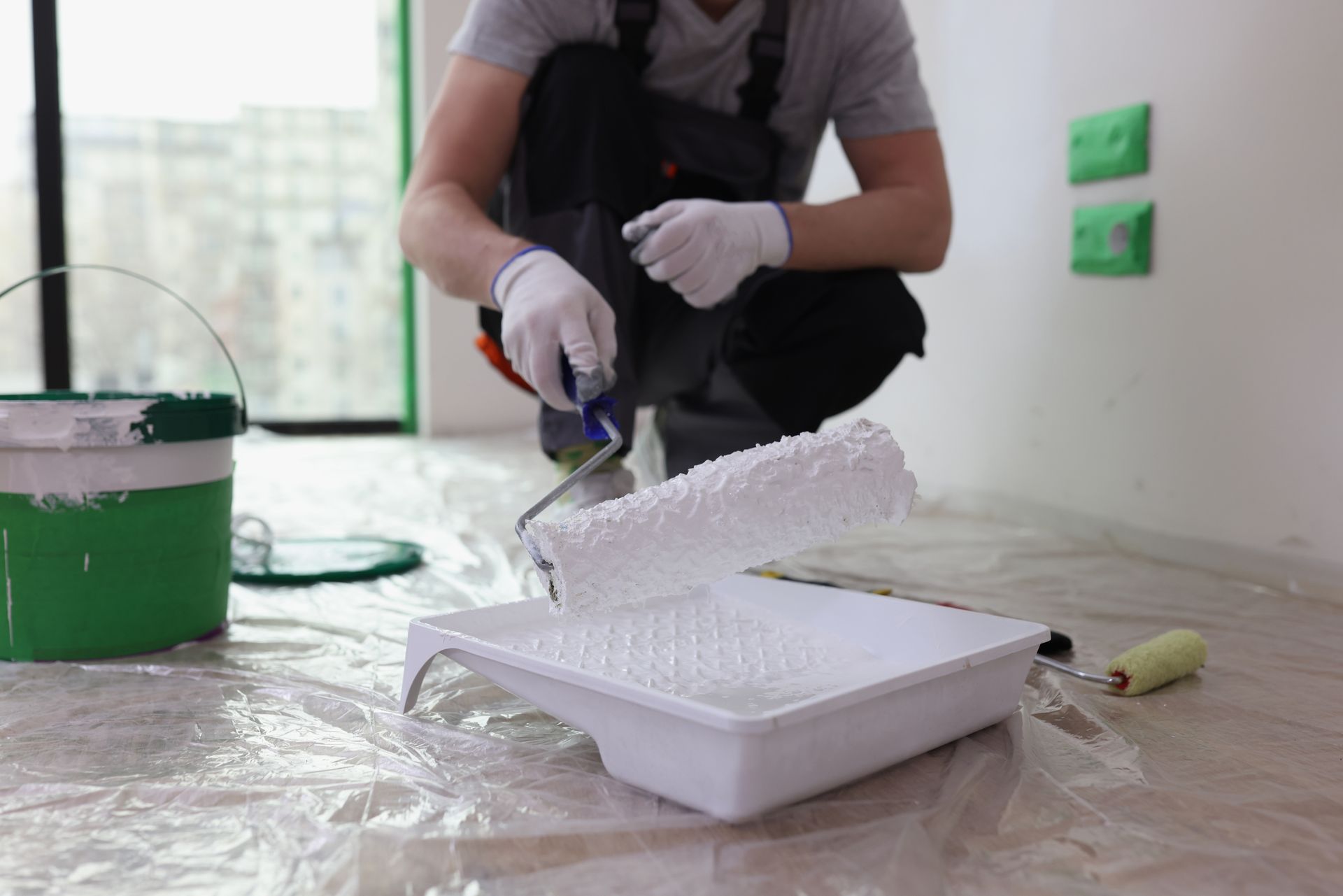Person painting a small white foam box on a drop cloth beside a green paint bucket
