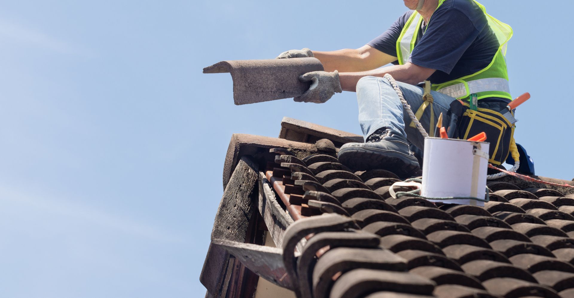 Roofing worker installing tiles on a house roof under a blue sky