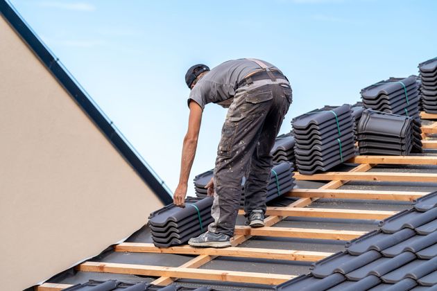 Worker installing roof tiles on a sloped roof under a blue sky