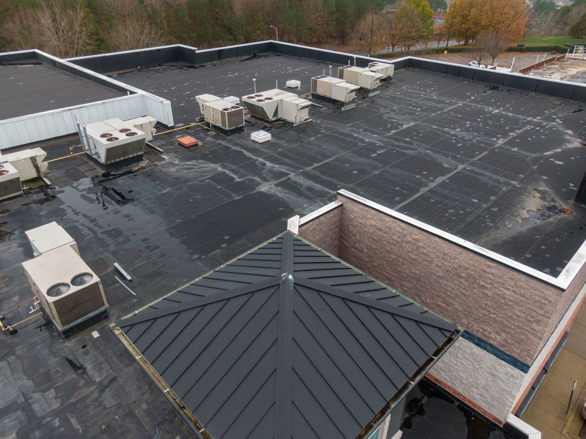 Rooftop with multiple HVAC units and a dark metal roof section on a brick building.
