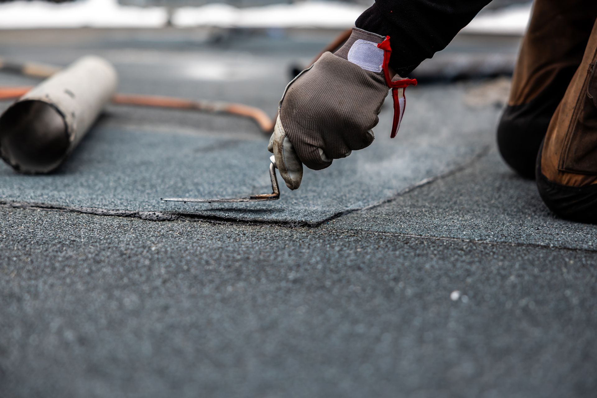 Roofing worker applying sealant to a flat roof with a caulking gun