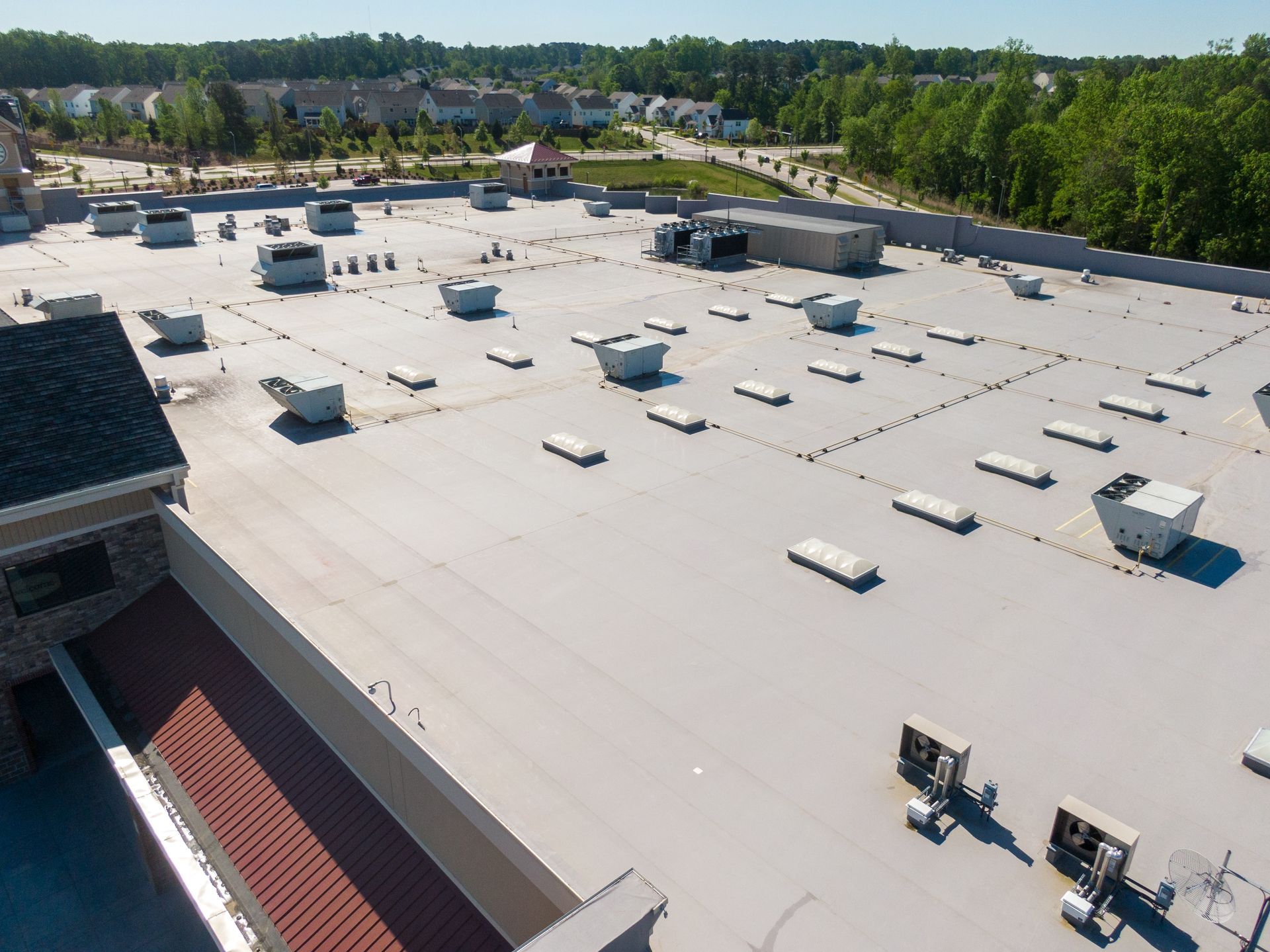 Aerial view of a large white flat rooftop with vents and HVAC units, surrounded by trees and buildings.