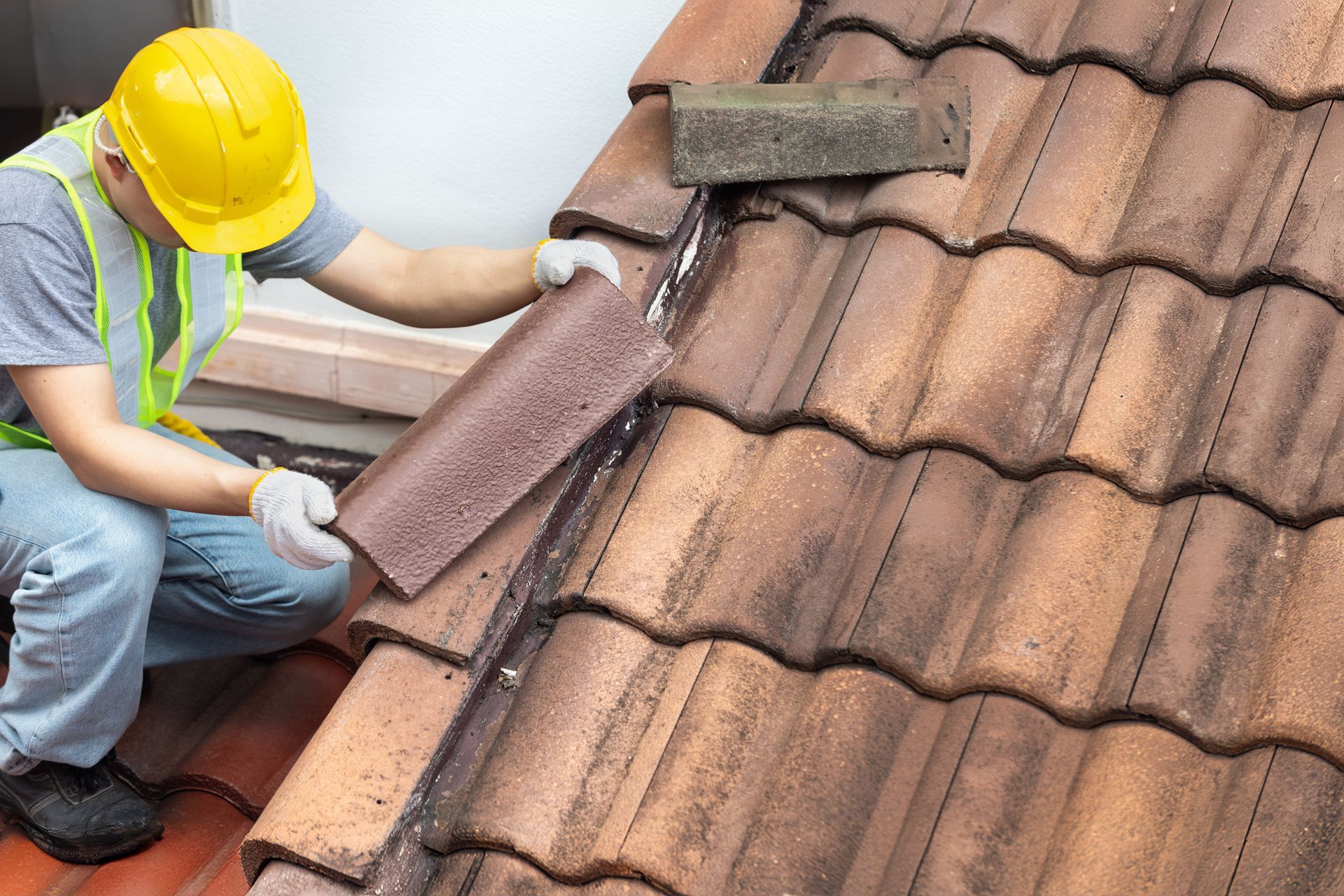 Worker in yellow hard hat repairing a tiled roof with a trowel