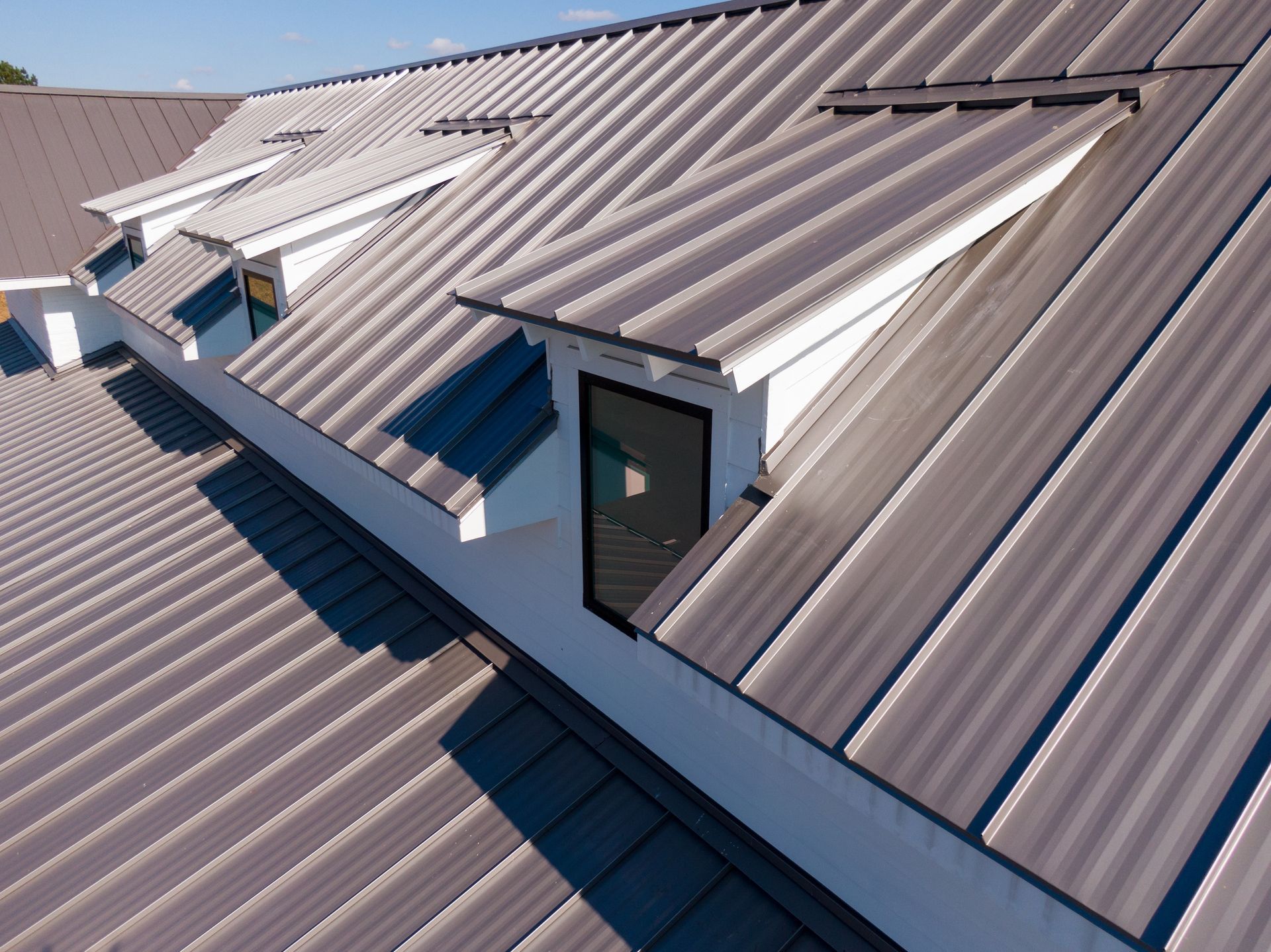 Rooftop with gray metal panels and multiple skylights under a clear blue sky