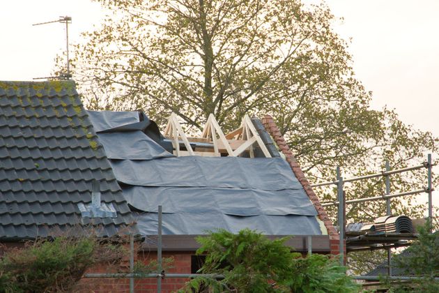 Damaged house roof with missing tiles and exposed wooden beams under repair