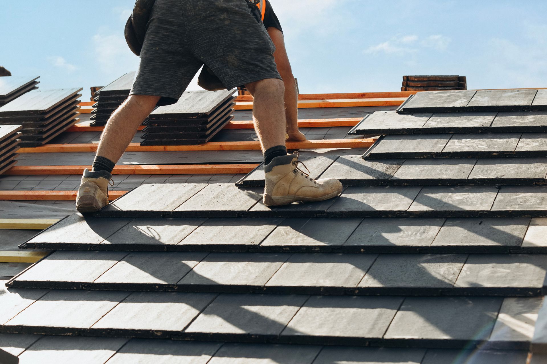 Worker installing shingles on a roof, with stacked materials visible in the background