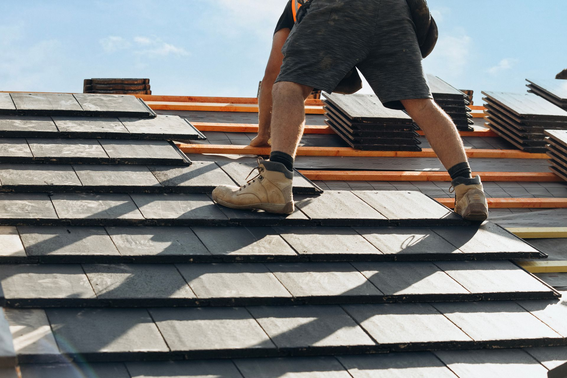 Worker installing shingles on a sloped roof under a bright sky