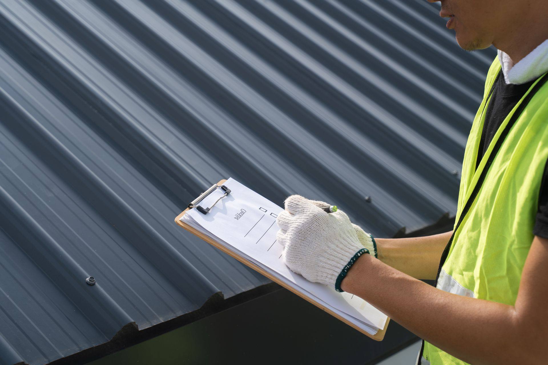 Worker in a neon safety vest writing on a clipboard beside a corrugated metal wall