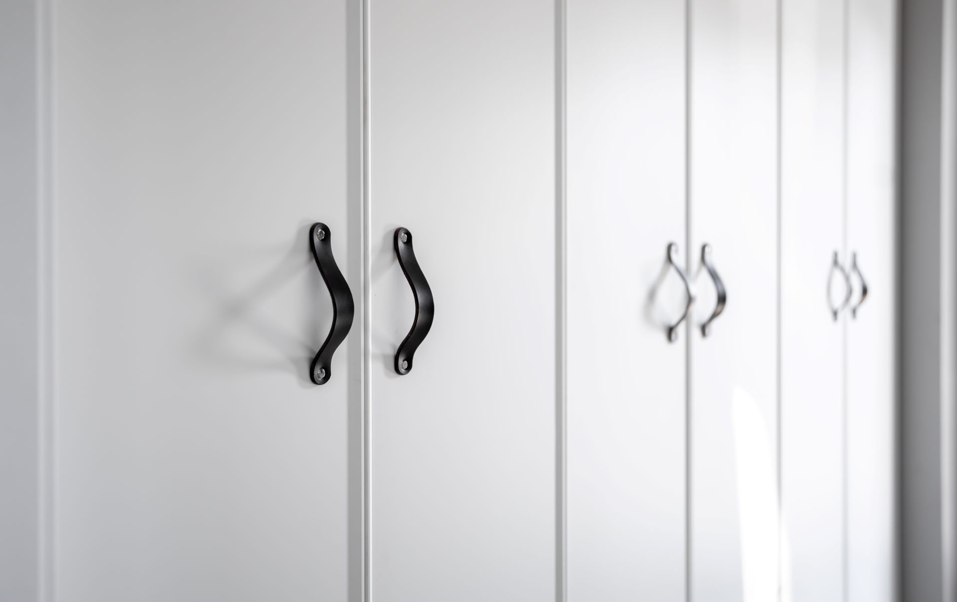 A row of white cabinets with black handles.