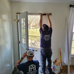 Two men are working on a door in a room.