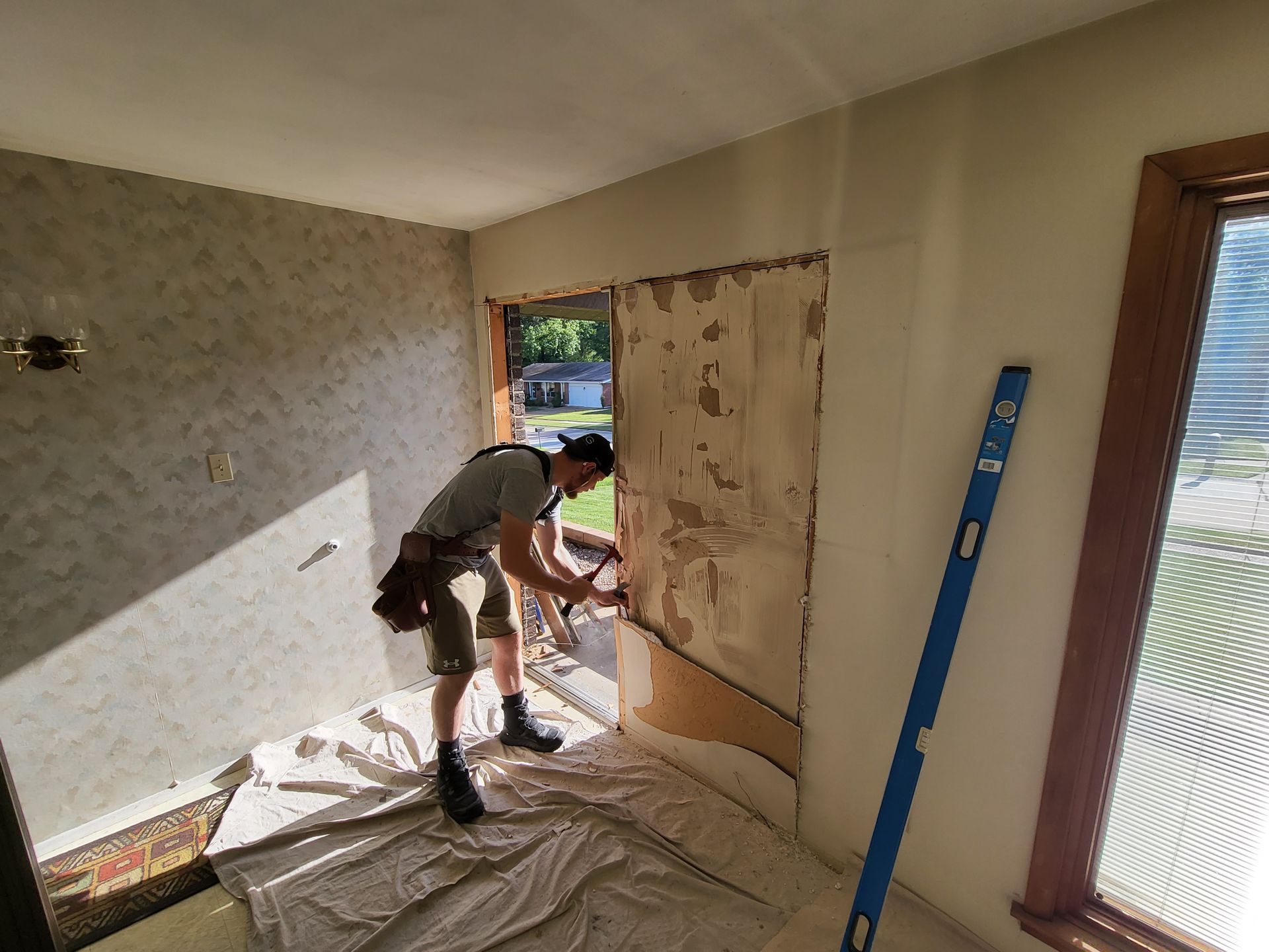 A man is working on a wall in a room next to a window.