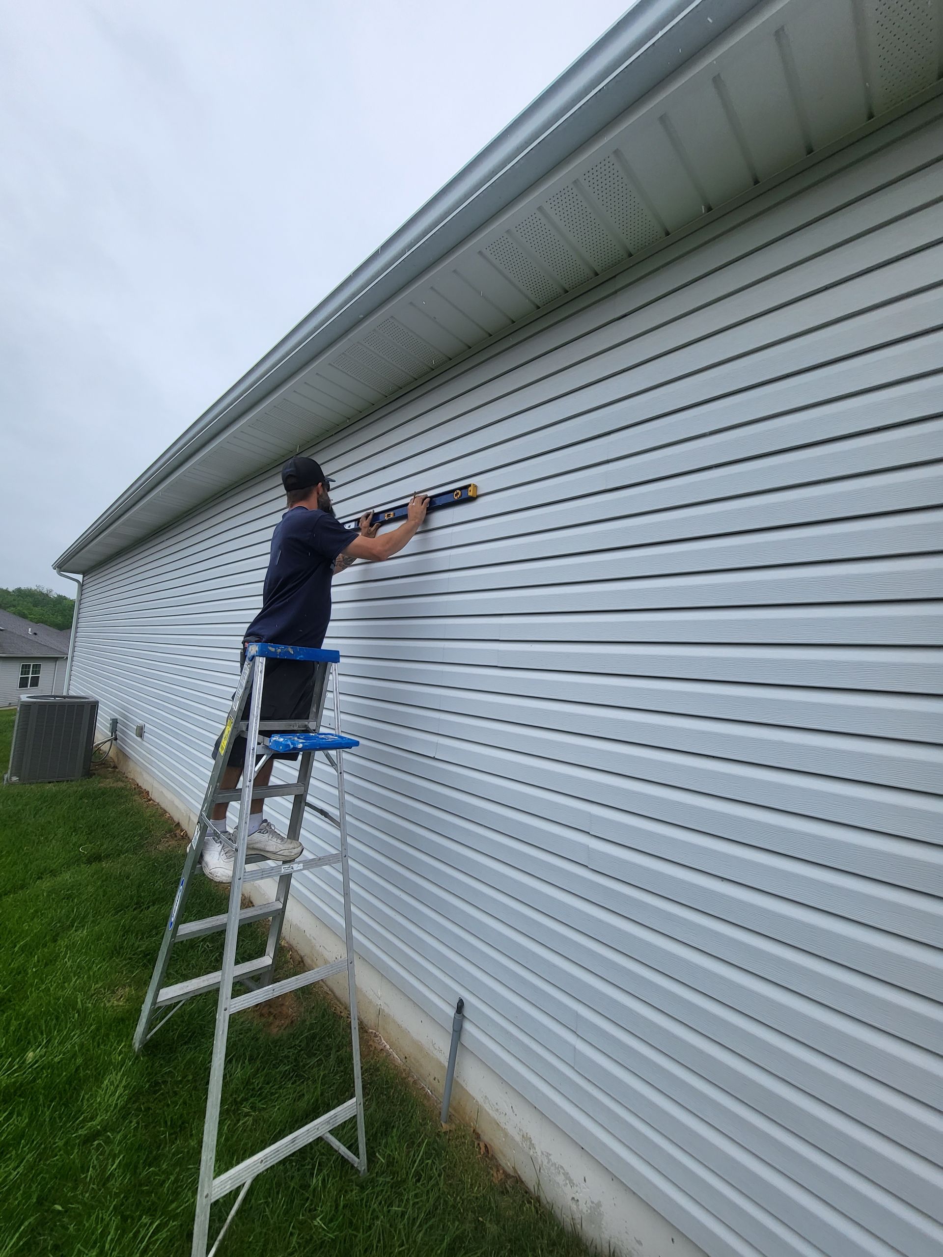 A man is standing on a ladder painting the side of a house.