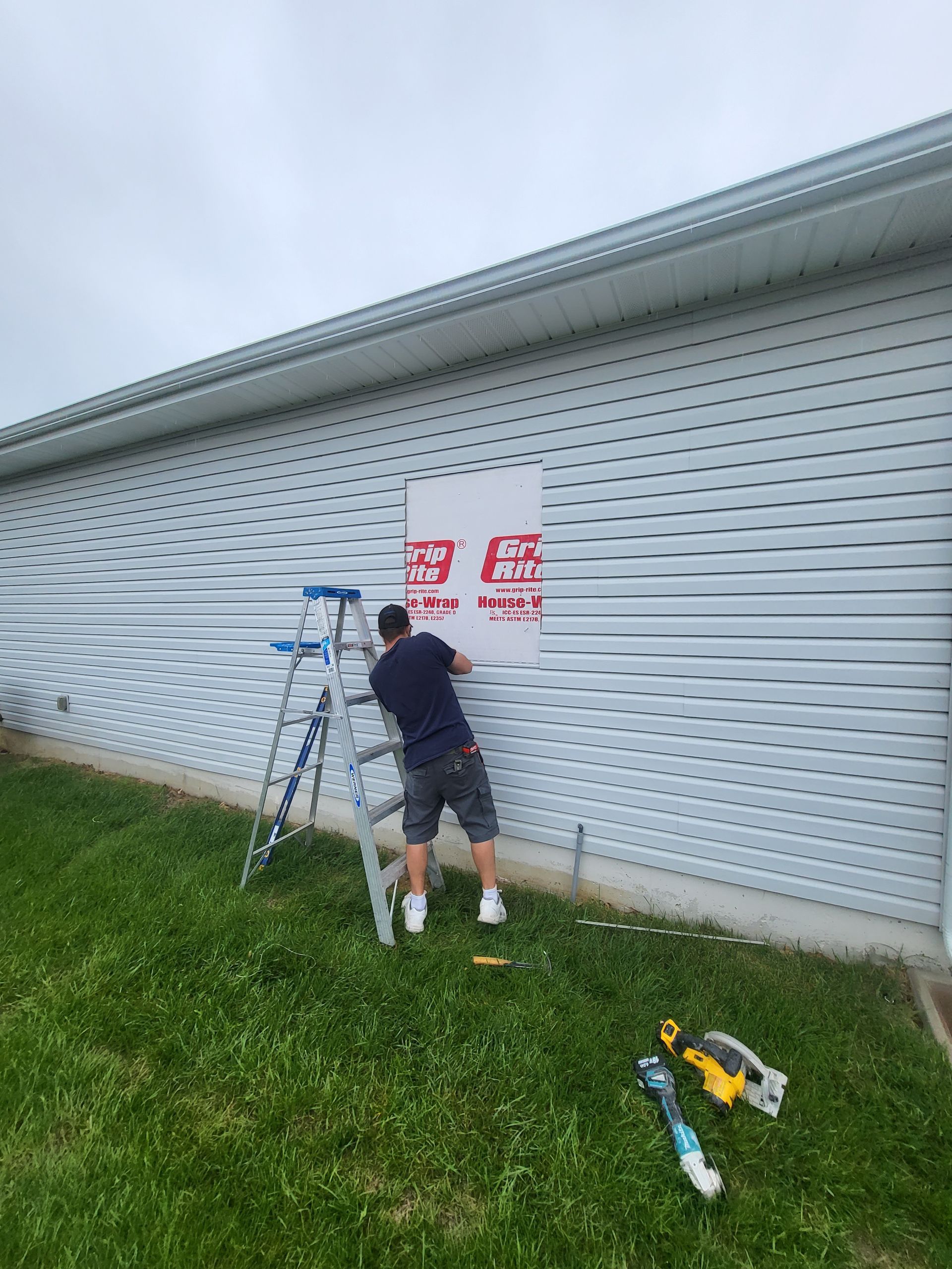 A man is standing on a ladder painting a sign on the side of a building.